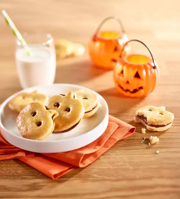 Halloween-themed cookies on a plate with milk and pumpkins in the background.