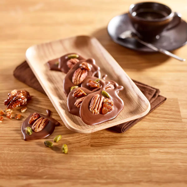 Chocolate-dipped treats with nuts on a wooden plate next to a cup of coffee.