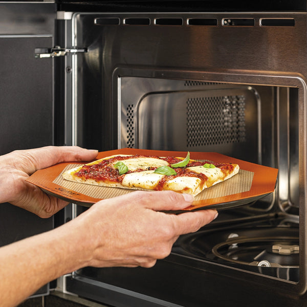 Person placing a pizza on a stone into an open oven.